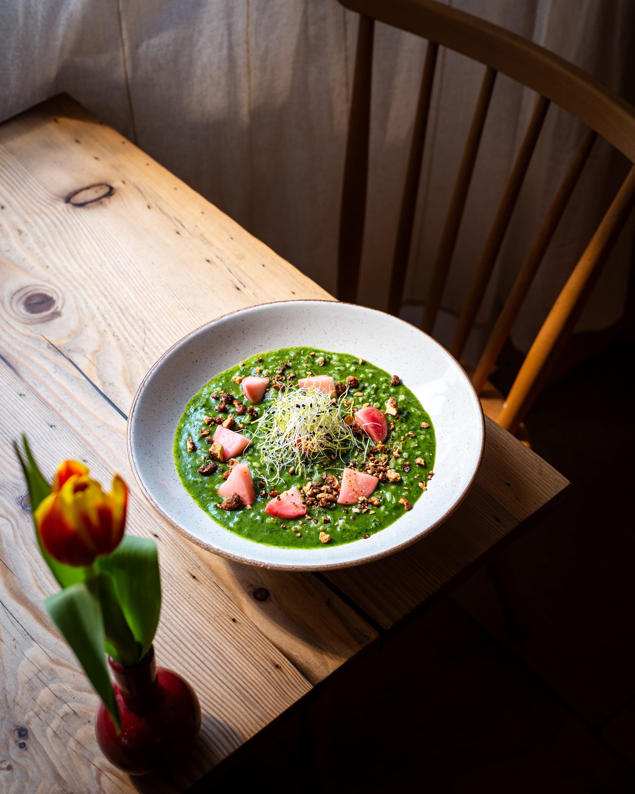 Green soup on a wooden table beside a tulip