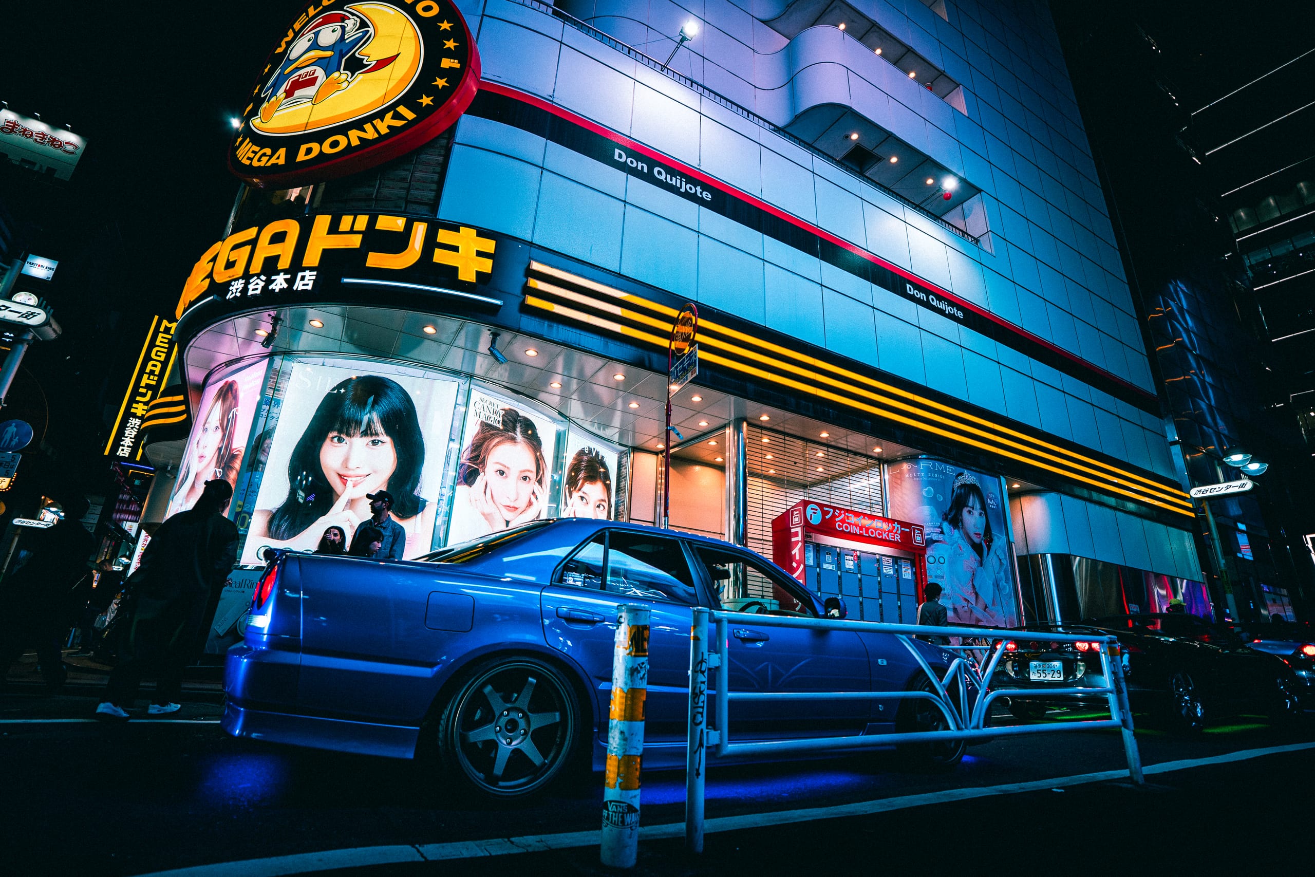 Blue Nissan Skyline parked beneath a neon-lit department store