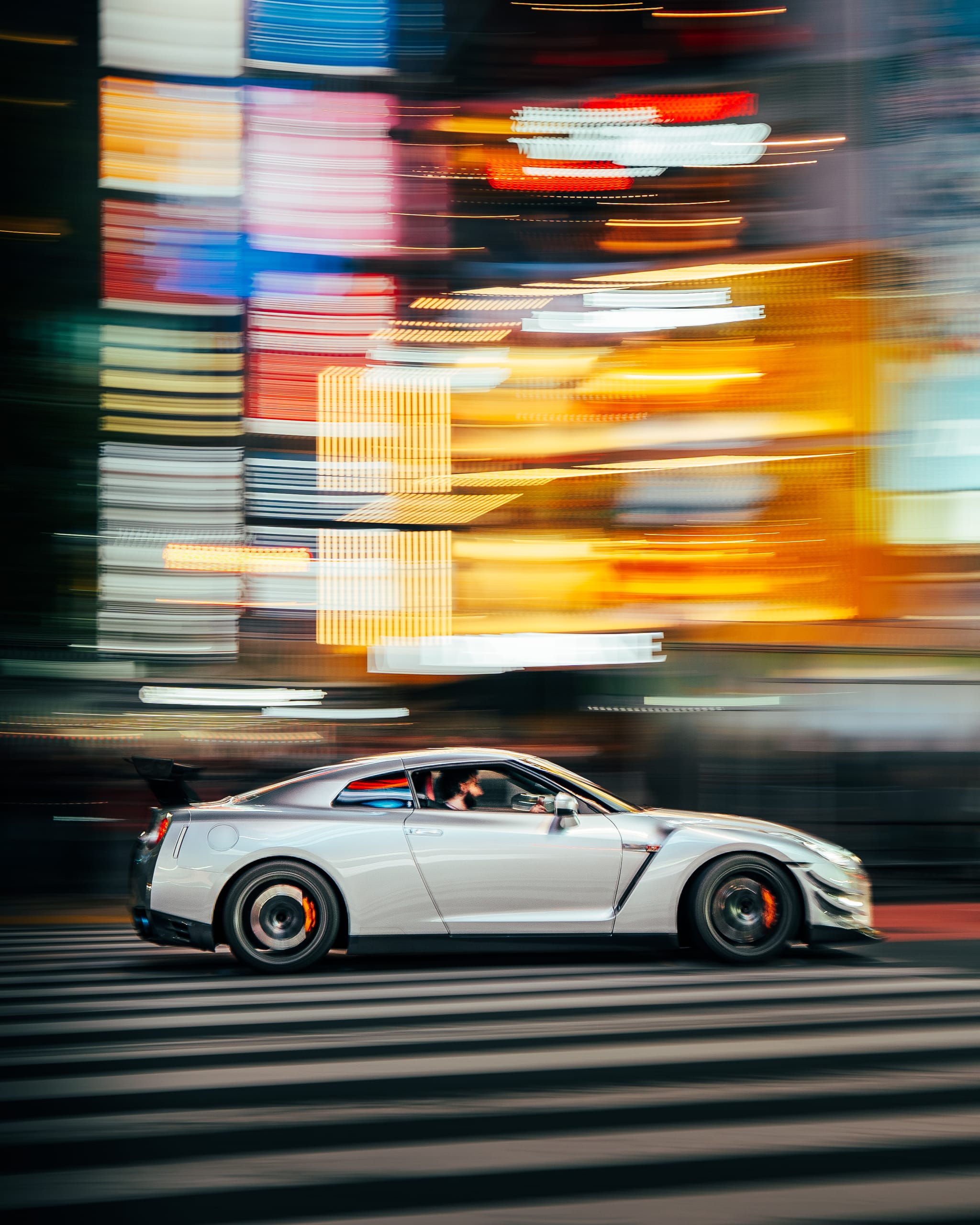 Silver Nissan GT-R streaking past neon signs in motion blur