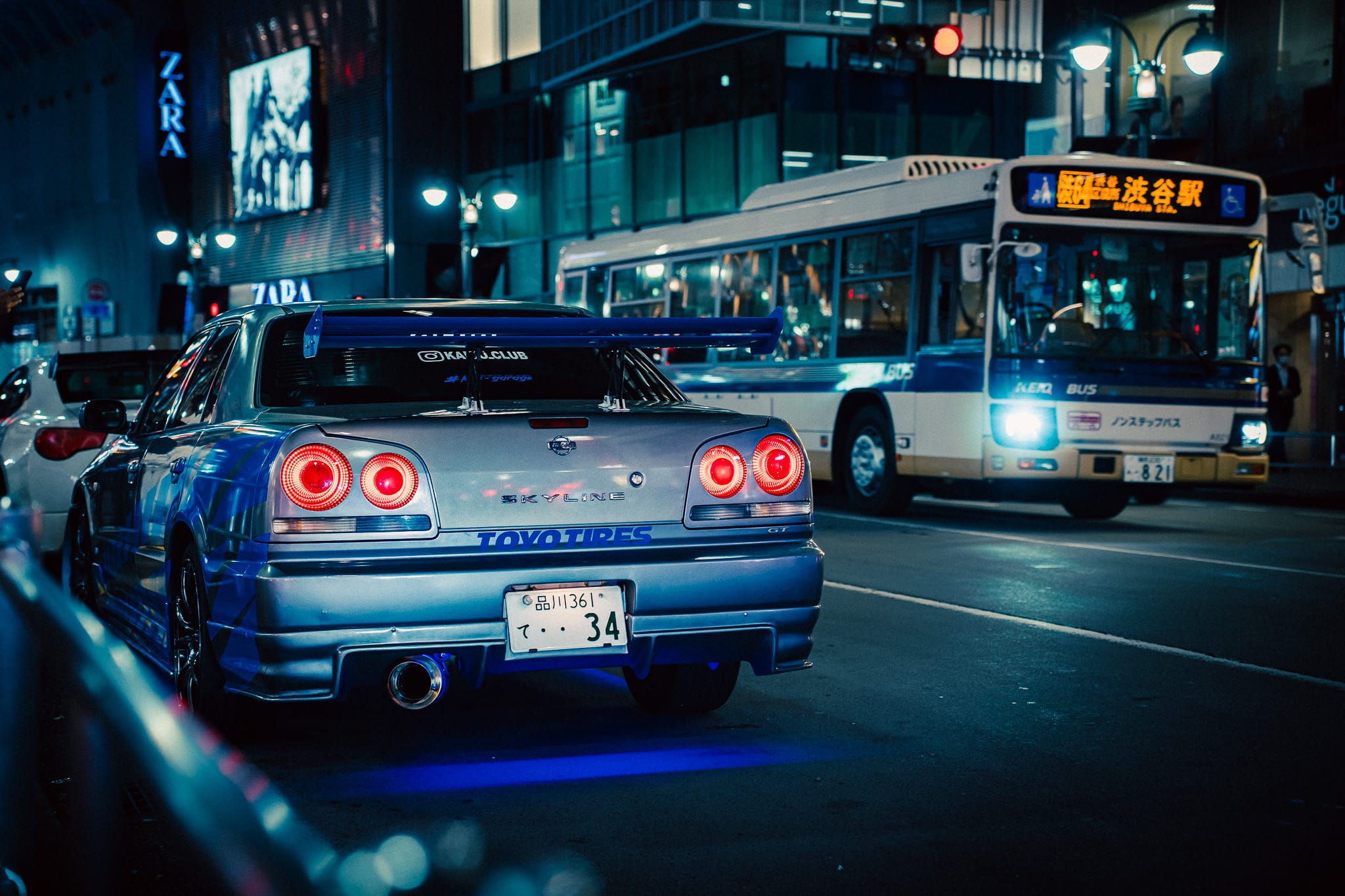 Blue Skyline R34 beside a city bus on a night street