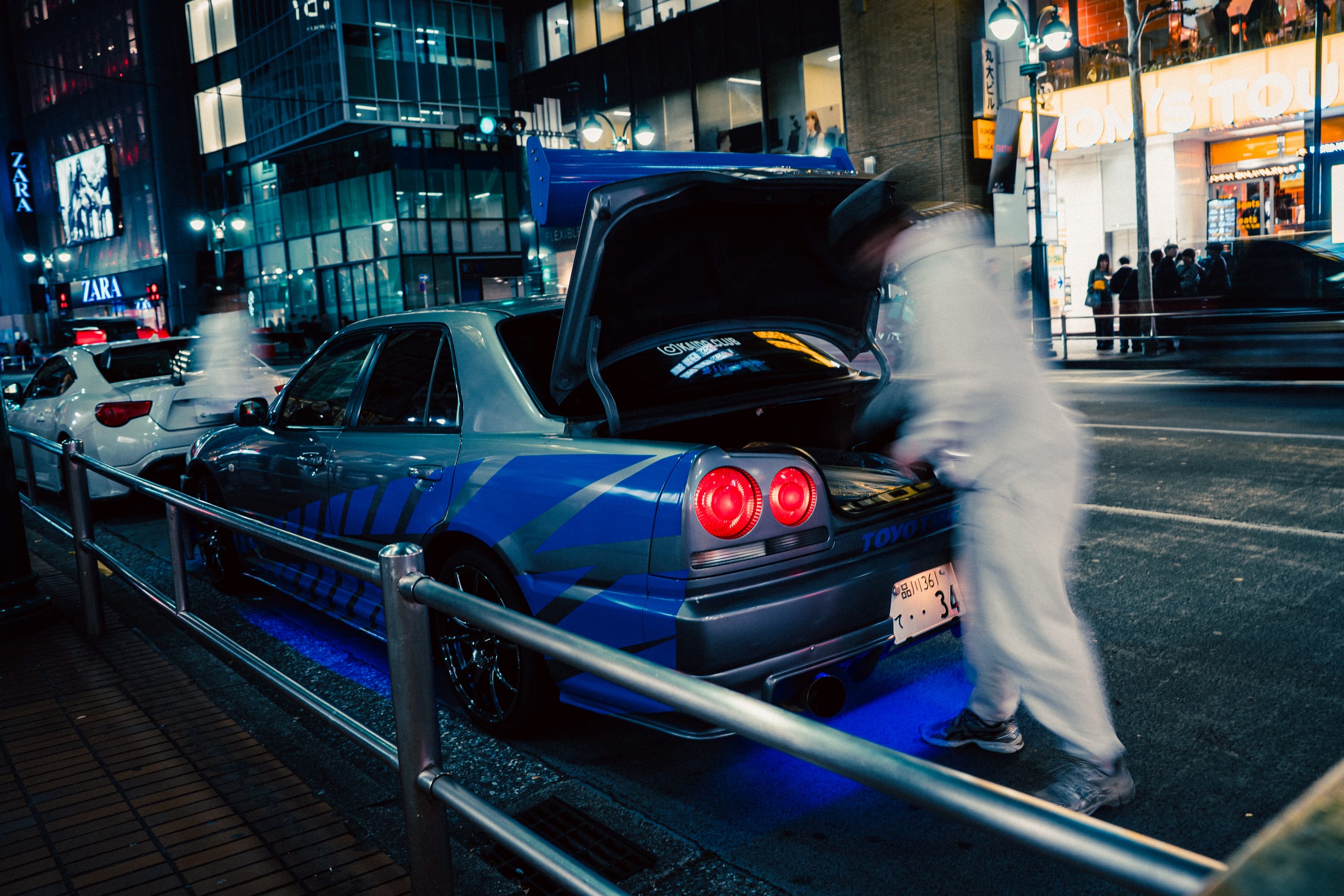 Driver at the open boot of a blue Skyline under city lights