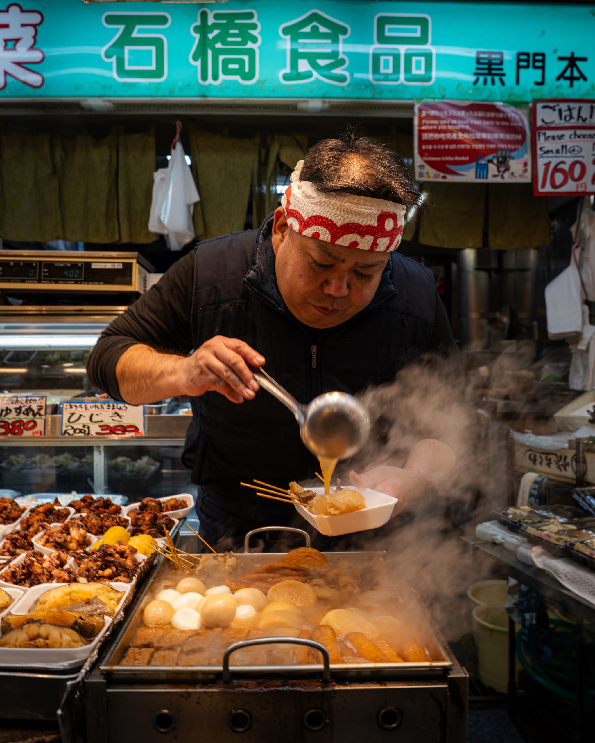 Street cook in a headband ladling broth at a market stall