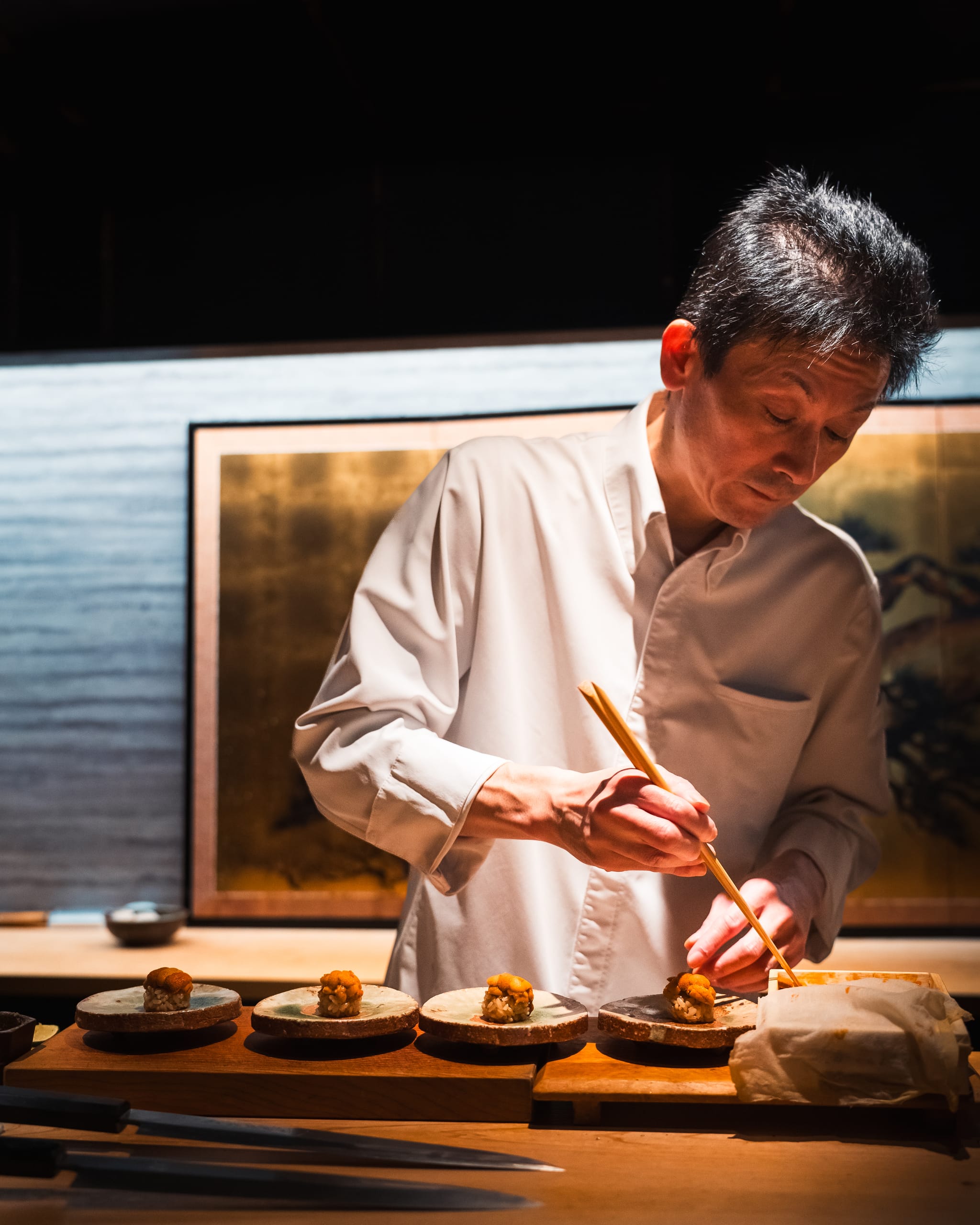 Chef plating with chopsticks at a counter