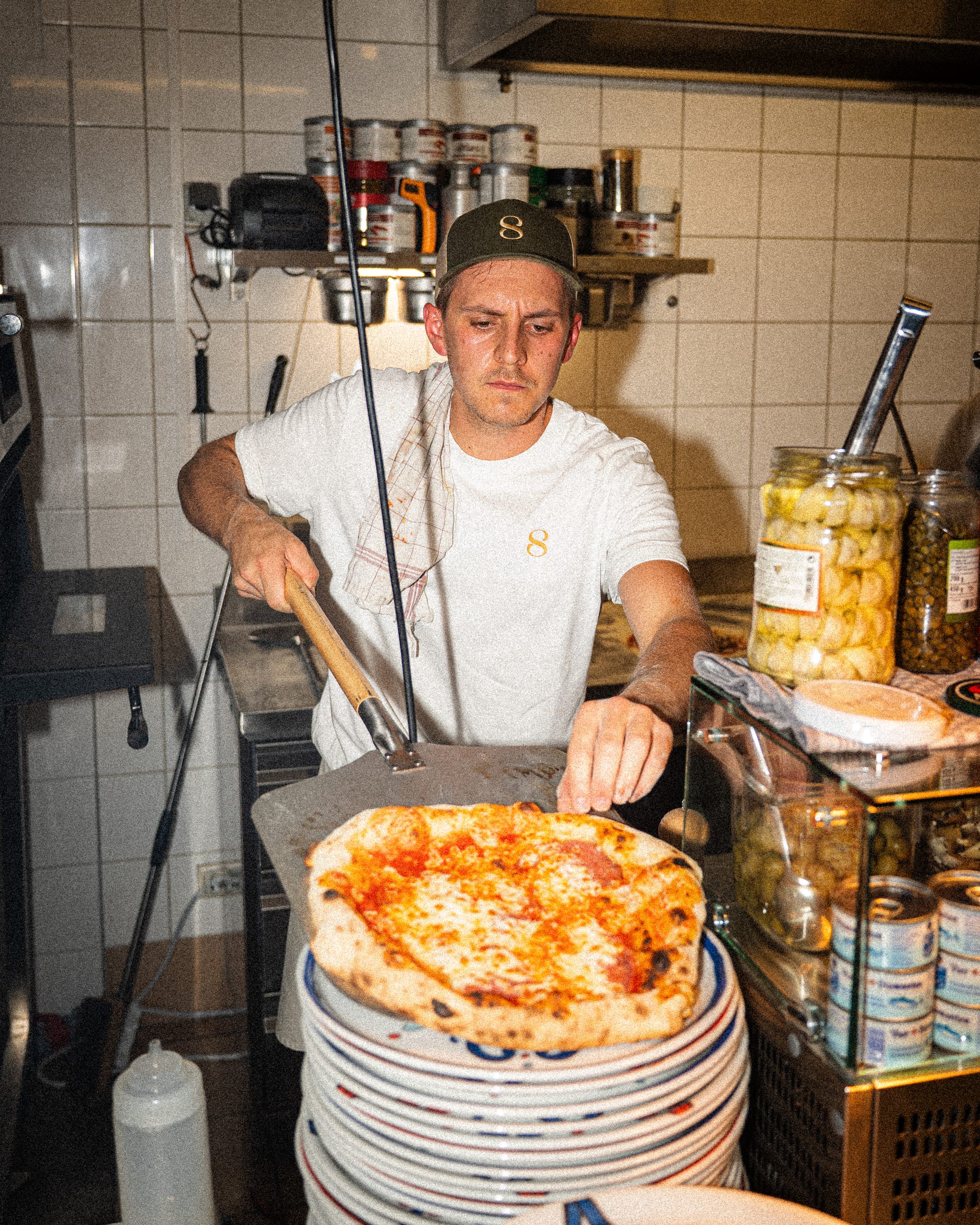Pizzaiolo sliding a pizza onto a stack of plates