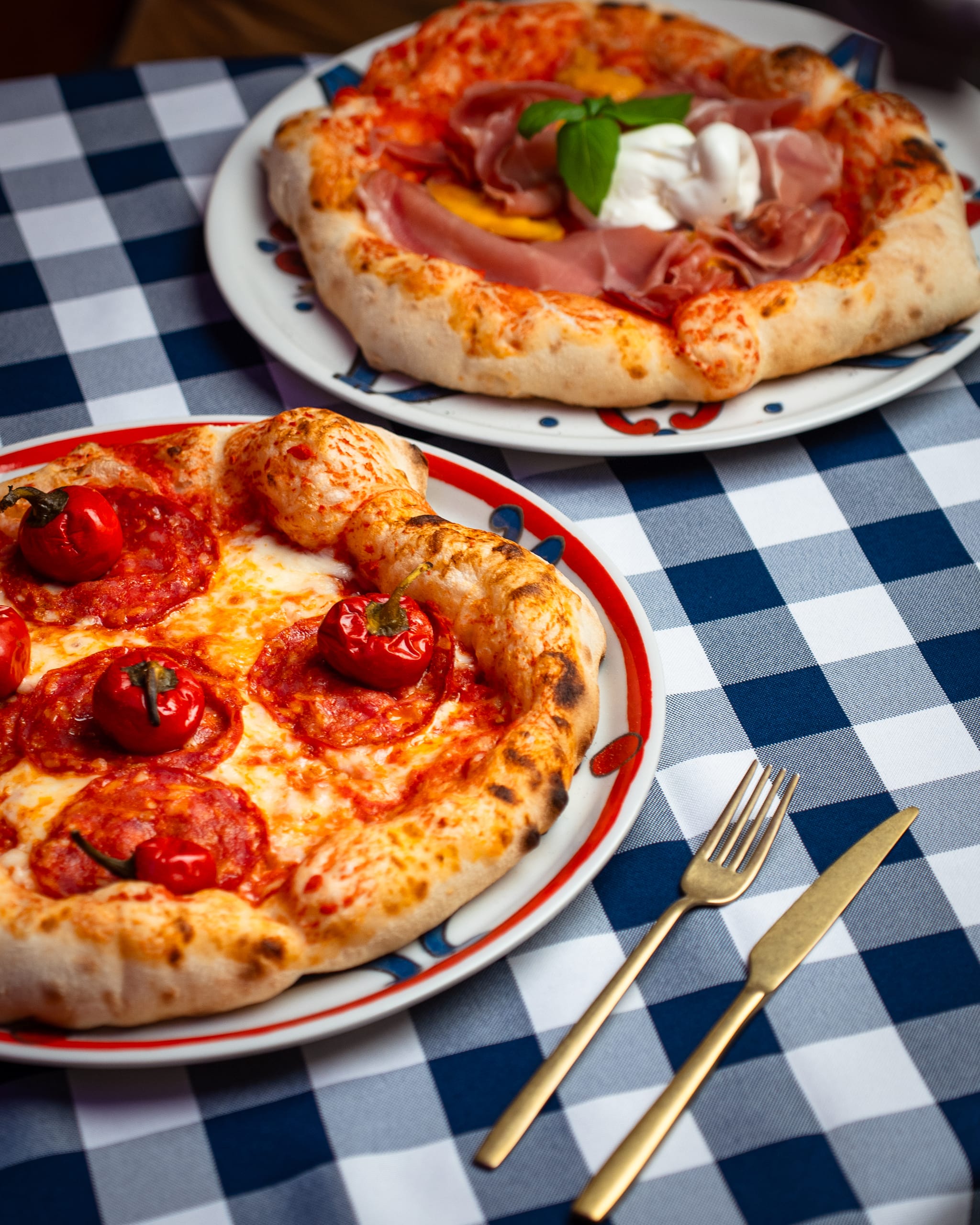 Two pizzas with prosciutto and burrata on gingham