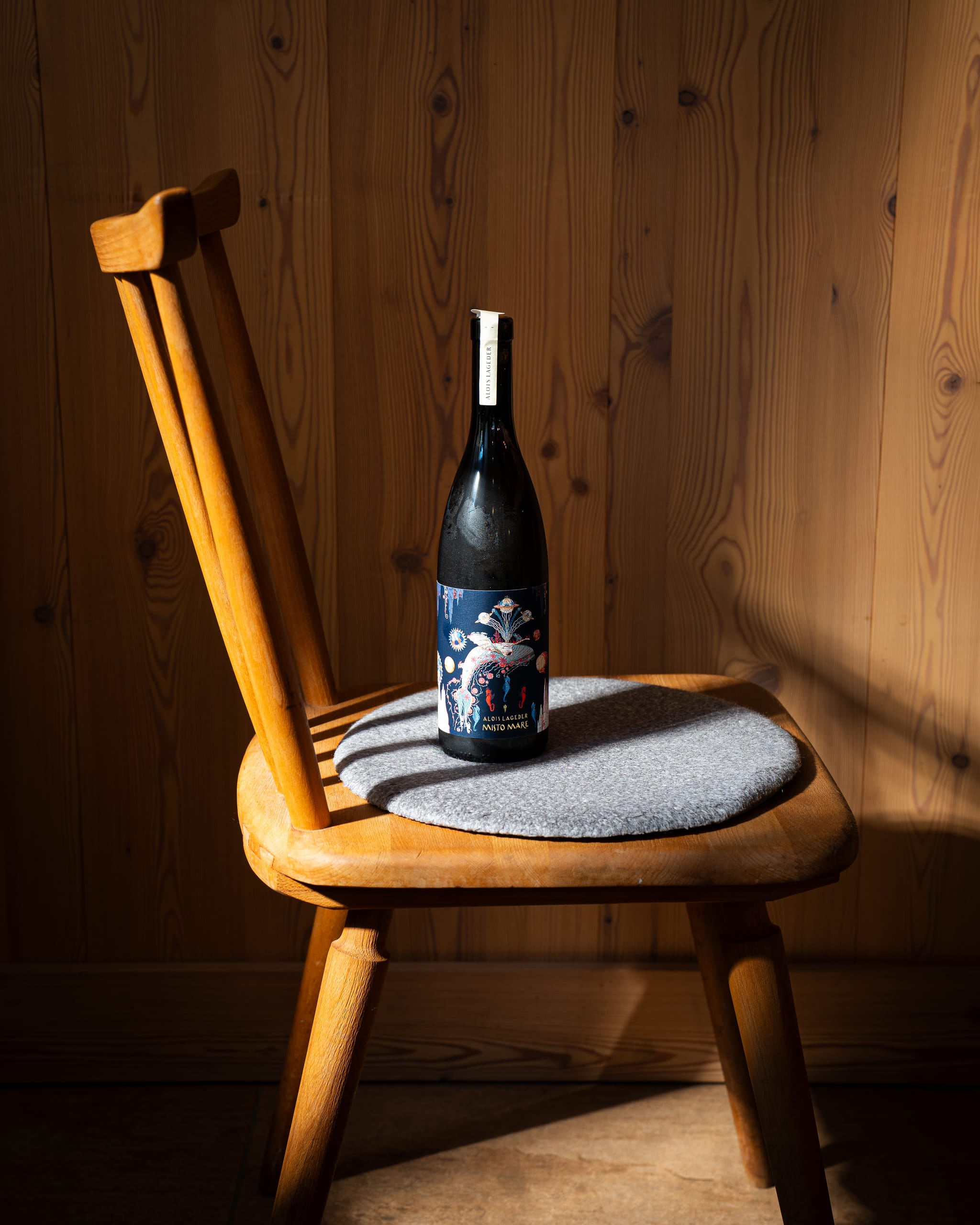 Dark wine bottle on a wooden chair in hard light