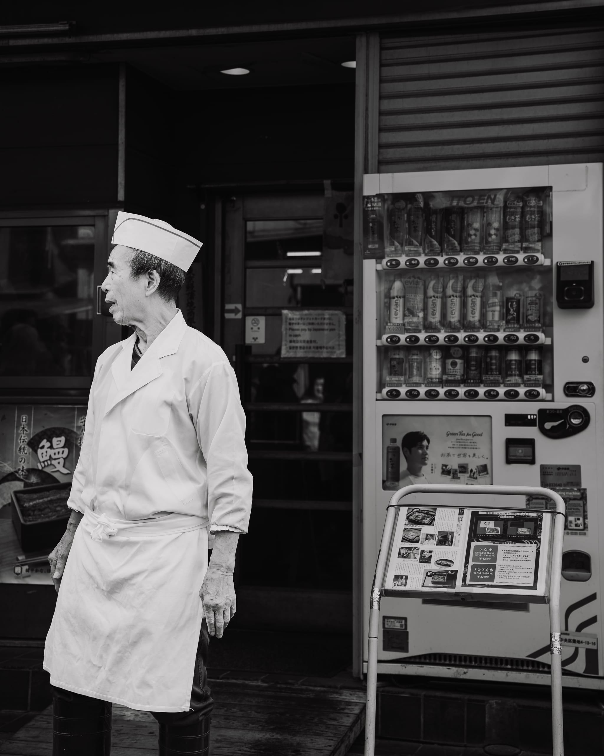 Chef in whites beside a vending machine, black and white